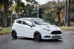 a white car parked on the side of a road in front of trees and grass