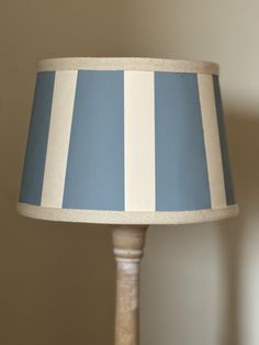 a blue and white striped lamp shade on a wooden table next to a beige wall