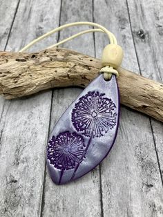 a purple dandelion pendant hangs from a piece of driftwood on a wooden table