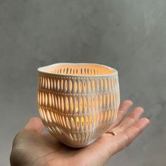 a hand holding a small white vase with wavy lines on it's side and light inside