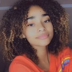 a close up of a person wearing an orange shirt with curly hair and blue eyes