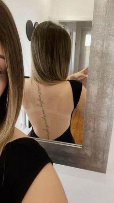 a woman looking at her back in front of a mirror with writing on the back