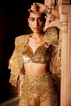 A bold three piece dress in sheer fabric, a glamorous embellished gold bralet paired with sheer trousers with splatter embroidery of sitara/patra and a matching sheer jacket with power shoulder highlighted with gold embellishments Fitted Sharara With Cape Sleeves For Festivals, Festive Chic Sharara, Evening Sets With Mirror Work In Organza, Diwali Sequin Set With Cape Sleeves, Bollywood Style Sequined Lehenga For Party, Glamorous Sequined Lehenga For Celebration, Glamorous Fitted Organza Choli, Festive Gold Embellished Choli, Glamorous Lehenga With Mirror Work For Celebration