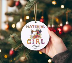 a hand holding a christmas ornament that says material girl with a sewing machine on it