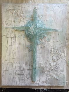 a cross painted on top of a piece of wood with white and blue paint over it