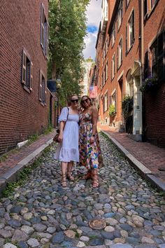 two women standing on cobblestone street next to brick buildings and an american flag