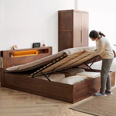 a woman unpacking a bed in a room with wood flooring and white walls