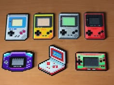 six different colored nintendo gameboys are arranged on a wooden surface, each with an 8 bit video game