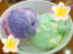 two scoops of ice cream in a white bowl with flowers on the table next to it