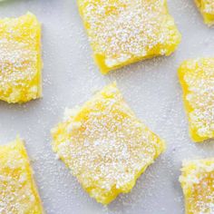 lemon squares with powdered sugar on top sitting on a white surface next to green leaves