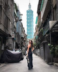 a woman walking down an alley way holding a skateboard in her hand and looking at the camera