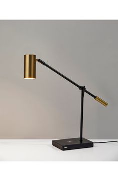 a black and gold lamp on a white table next to a gray wall with a yellow light