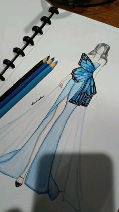 a drawing of a woman in a blue dress with pencils next to it on a notepad