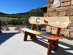 a snowboard sitting on top of a wooden bench next to a stone building with mountains in the background