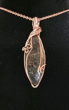 The pendant features a polished, elongated dinosaur bone fossil encased in an elegant wire wrap setting. The copper wire is intricately twisted and forms decorative loops around the stone, providing an artistic touch. The pendant hangs from a matching chain, highlighting the fossil's natural patterns and textures. Pendant length: 2 inch Matching copper chain included Dino bone cabochons are gemstones made from the fossilized remains of dinosaur bones.  These stones are created when minerals like silica, quartz, or agate replace the bone tissue over millions of years, forming a fossil with stunning colors and patterns. Dino bone cabochons are favored in jewelry-making because of their striking appearance and the unique story each piece. The fossilized bone gains the hardness and durability Bone Tissue, Prehistoric Dinosaurs, Natural Patterns, Bone Pendant, Dinosaur Bones, The Bone, Aesthetic Beauty, Copper Chain, Patterns In Nature