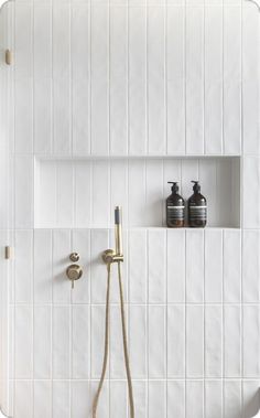 a white tiled bathroom with two shower heads and soap dispensers on the wall