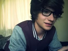 a young man wearing glasses sitting in front of a laptop computer