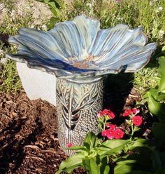 a blue vase sitting on top of a flower bed next to some red and white flowers