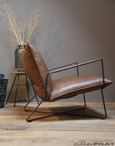 a brown leather chair sitting on top of a wooden floor next to a vase filled with flowers