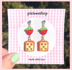 a pair of earrings with fruit on them sitting in front of a pink and white checkered background