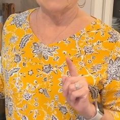 a woman in a yellow floral top pointing to the side with her finger and smiling at the camera