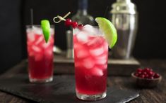 two glasses filled with red liquid and garnish on top of a wooden table