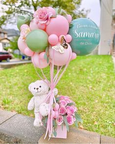 a bunch of balloons with a teddy bear and flowers in the center on a sidewalk