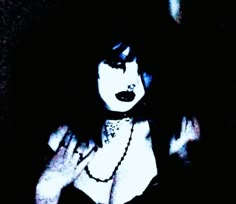 a woman with dark hair and black makeup is posing for the camera, her hands on her chest