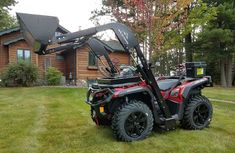 a can - am outlander parked in front of a log cabin on the grass