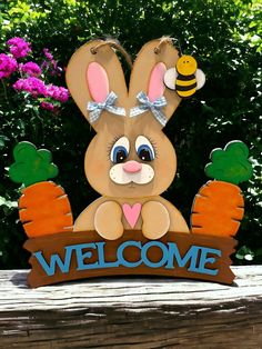 a wooden sign with a bunny holding carrots and a bee on it that says welcome