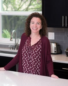 a woman standing in front of a kitchen counter with an oven and sink behind her