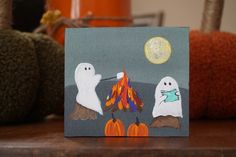 a card with two ghostes around a campfire on a table next to pumpkins