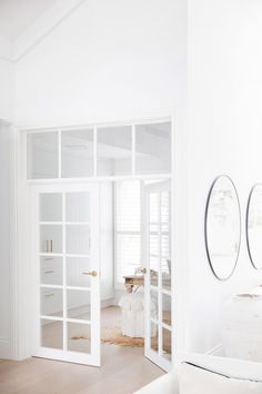 a living room with white walls and wooden floors, two mirrors hanging on the wall