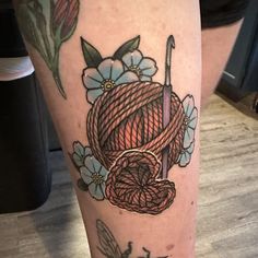 a tattoo on the leg of a woman with yarn and flowers