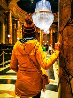 a woman in an orange jacket is looking at the chandelier