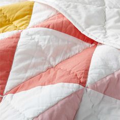 an unmade bed with pink, yellow and white quilts on top of it