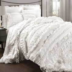 white ruffled comforter set on a bed in a room with wood flooring