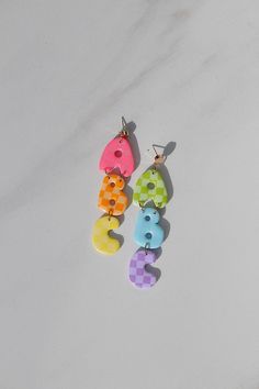 three pairs of multicolored wooden earrings on white marble counter top, with one pair dangling from the ear