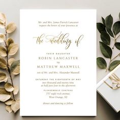 a wedding card with gold foil on it next to some leaves and a gift box