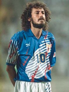 a man with long hair wearing a blue shirt and white shorts standing on a soccer field