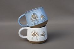 two mugs stacked on top of each other with trees painted on the cups and sides