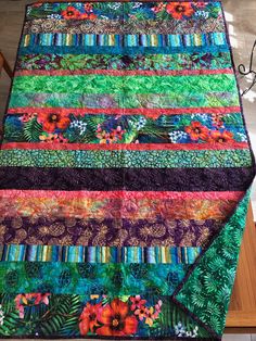 a multicolored quilt with flowers and leaves on the bottom, sitting on top of a wooden table