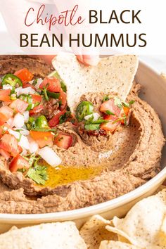 a hand dipping a tortilla chip into a bowl of black bean hummus