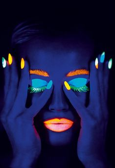 a woman's face with bright makeup and neon lights painted on her hands over her eyes