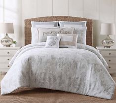 a bed with white comforter and pillows on top of it in front of two lamps