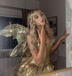 a woman dressed as a fairy in front of a mirror holding her hand up to her face