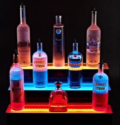 an assortment of liquor bottles sitting on top of a neon lit shelf in front of a black background