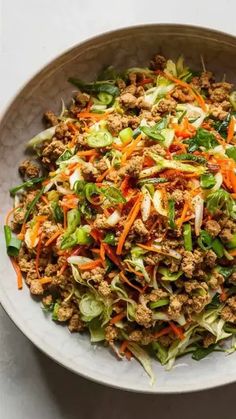 a white bowl filled with lettuce, carrots and ground beef mixed in