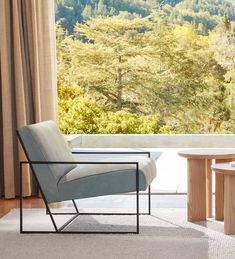 a chair and table in front of a large window with trees outside the windowsill