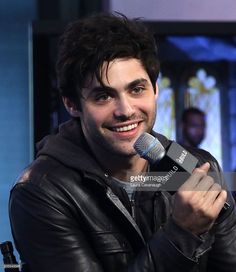 a man holding a microphone in his right hand and smiling at the camera while wearing a black leather jacket